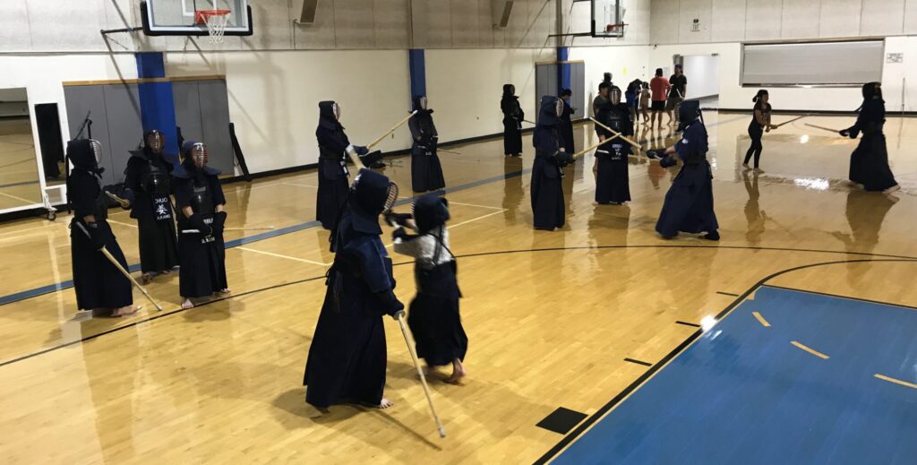 A typical evening session at Norwalk Kendo Dojo. Students wait to spar and learn from their head instructor Kodama. Here, Kodama is currently sparring and instructing a child.