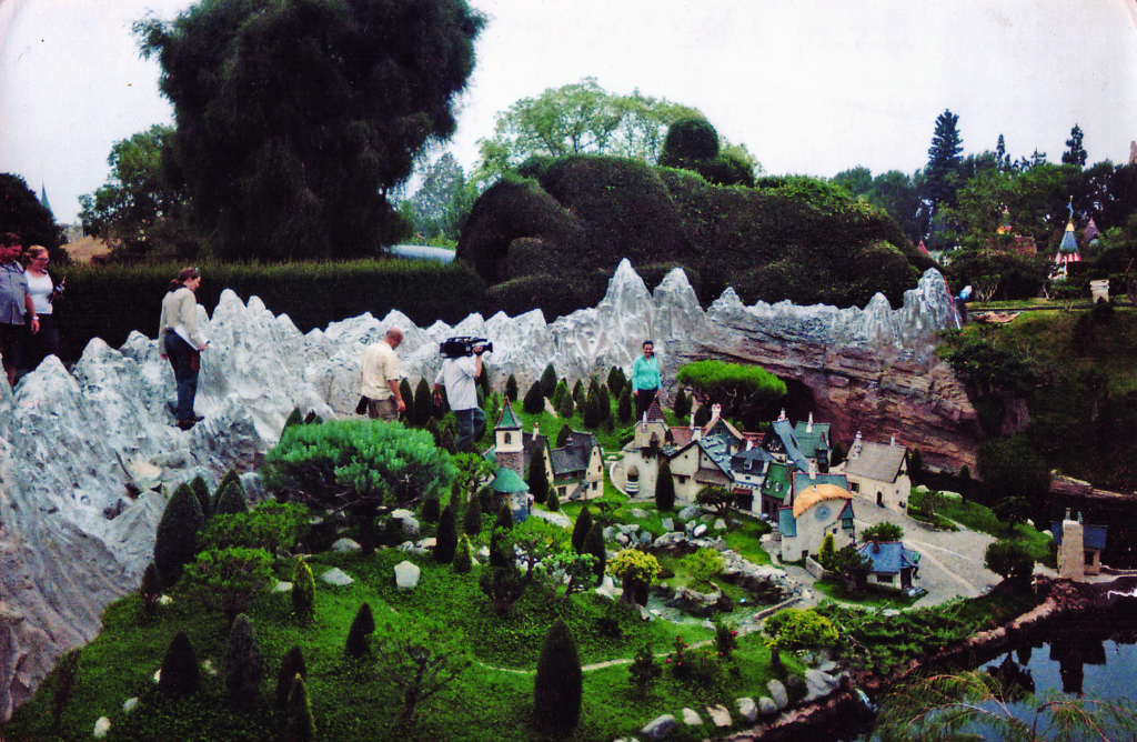 The "Walt Disney tree," a Swiss Mountain pine, in Storybook Land. This bright green tree is to the right of the woman in blue, near her left arm. Dennis was hired to bring the tree back to health and style it to look like a type of tree that grows in the Alps. The woman in blue was the video director.